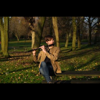 James sitting outside among trees playing a Scottish traditional flute