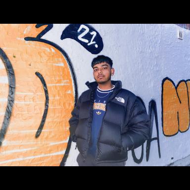 Joash standing outside in front of white wall spray painted with black and orange