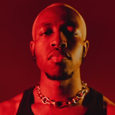 Headshot of Khalil wearing a chain and black vest, lit by red light