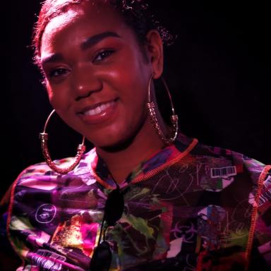 Rianne wearing patterned top and hoop earrings, lit by red light