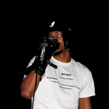 dochi wearing a white t-shirt and black cap holding a microphone