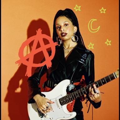 Svetlana holding a white guitar and posing against an orange background