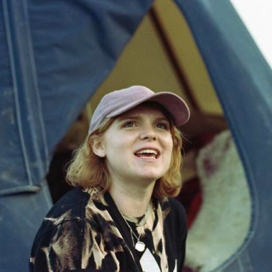 Woman with blonde hair wearing grey baseball cap and brown patterned jacket looks up away from camera