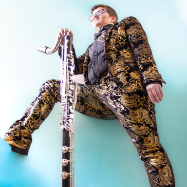 a person in a patterned suit poses with a clarinet
