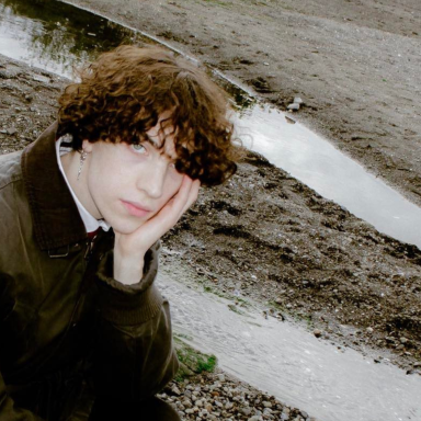 garrett has brown curly hair and wears a green jacket and looks at the camera. a wetland is behind him.