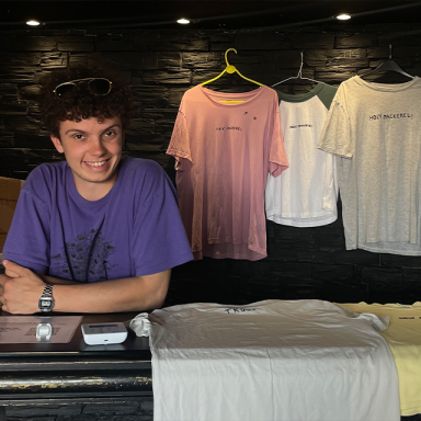james smiles and wears a purple t-shirt. he is standing at a merch stand