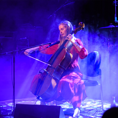 maddie sits on stage and plays the cello in indigo lighting