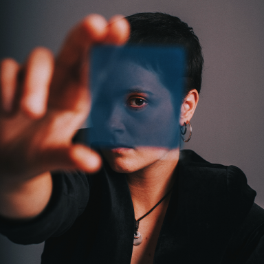 a person with short dark hair holds up a blue transparent square to the camera