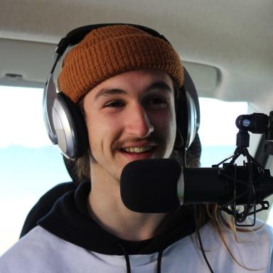 a man wears a brown beanie and headphones in front of a mic