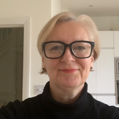 a woman with short platinum hair wears red lipstick and black glasses with a black turtleneck
