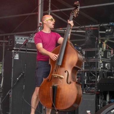 a man in a red top and shorts plays cello on stage