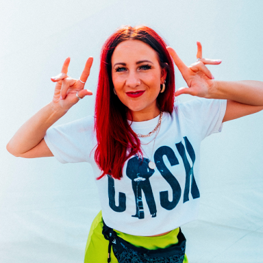 a woman with red hair and a white t shirt poses with her hands in rock signs