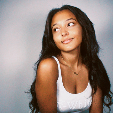 a woman with long dark hair and a white tank top looks to the side