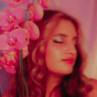 a woman closes her eyes and looks to the side; pink flowers are next to her face. there is a pink filter over the photo