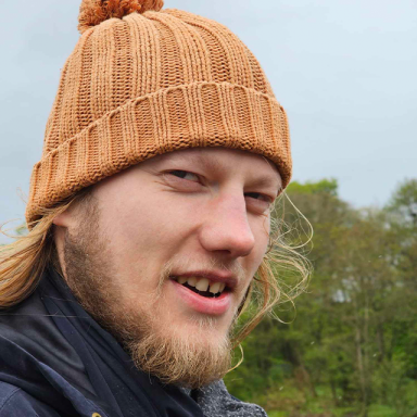 a man with blonde hair and a beard wears an orange bobble hat