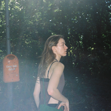 a person with brown hair and a black strappy top is seen by a bush